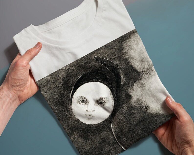 May include: White t-shirt with a black and white illustration of a child's face in a circle, surrounded by clouds.