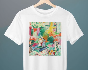 May include: A white t-shirt featuring a colourful painting of a woman reading a book in a garden setting. The painting uses vibrant colours, including green, blue, yellow, and pink.