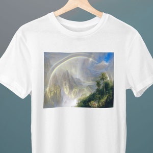 May include: A white t-shirt featuring a print of a painting depicting a lush green landscape with a waterfall and a rainbow in the sky.