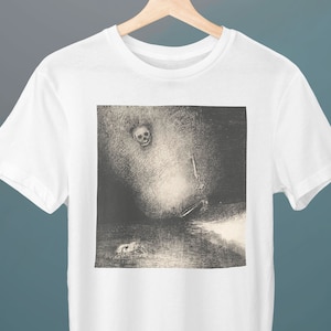 Puede incluir: Una camiseta blanca con una imagen en blanco y negro de una calavera y una figura en un paisaje oscuro y brumoso.