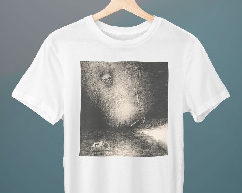 Puede incluir: Una camiseta blanca con una imagen en blanco y negro de una calavera y una figura en un paisaje oscuro y brumoso.