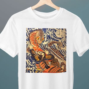 May include: White t-shirt featuring a colourful Japanese woodblock print of a mythical creature and a warrior in a wave. The print incorporates blue, red, orange, and black colours.