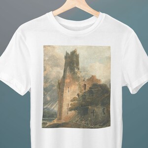 Puede incluir: Una camiseta blanca con una impresión de estilo vintage de una torre de piedra en ruinas sobre un fondo de cielo nublado.
