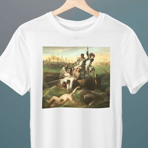 May include: A white t-shirt with a painting of a group of people in a boat being attacked by a shark. The painting is in a realistic style and depicts the scene in a dramatic way.