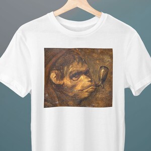 Puede incluir: Una camiseta blanca con una pintura vintage de la cara de un mono con una pipa en la boca. El mono es marrón y el fondo es de un marrón apagado.