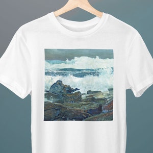May include: A white t-shirt with a graphic print of a seascape. The image shows a rocky coastline with crashing waves and a stormy sky.