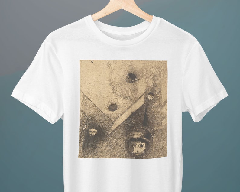 May include: A white t-shirt with a black and white print of a surrealist artwork. The artwork features multiple faces and a geometric design.