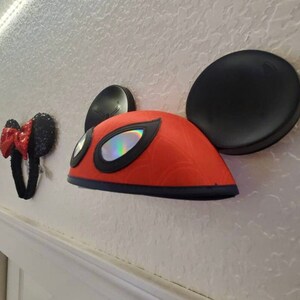 May include: Three pairs of character ears, including a red and black pair with a spider-man design, a black pair with a white bow, and a pink pair with a white bow.