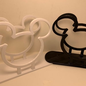 May include: Two Mickey Mouse-shaped napkin holders, one white and one black. The holders are made of plastic and have a simple design.