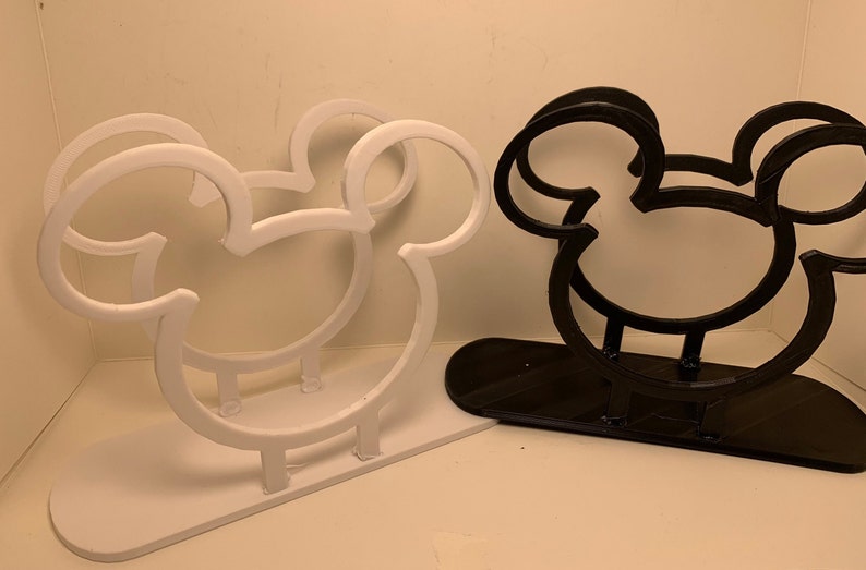 May include: Two Mickey Mouse-shaped napkin holders, one white and one black. The holders are made of plastic and have a simple design.
