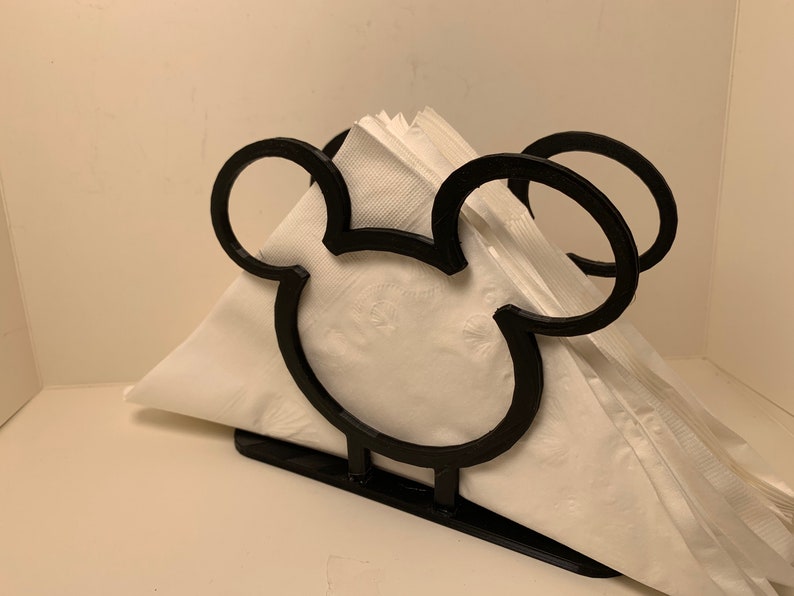 May include: Black metal napkin holder shaped like Mickey Mouse's head. The holder is empty and ready to hold napkins.