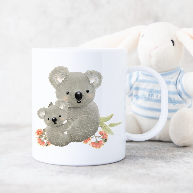 May include: White ceramic mug with a graphic of two koalas, a mother and baby, sitting on a branch with eucalyptus leaves and pink flowers.