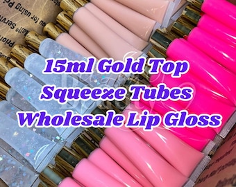 May include: A collection of 15ml squeeze tubes with gold caps, containing various lip glosses in clear with glitter, light pink, and bright neon pink colors, arranged in a cardboard box with the text 15ml Gold Top Squeeze Tubes Wholesale Lip Gloss.
