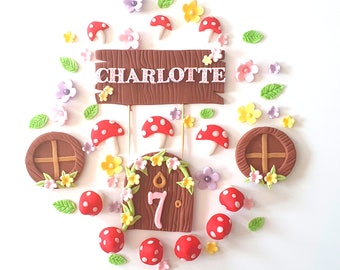 May include: A whimsical cake decoration set featuring a brown wooden sign with the name "CHARLOTTE", a fairy door with the number "7", red mushroom accents, flowers, and green leaves. The set is designed for a birthday cake.