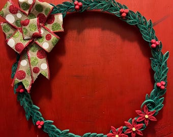 May include: A handmade Christmas wreath with a green paper filigree design. The wreath features red berries, a red and white polka dot bow, and red flowers. The wreath is set against a red background.