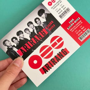 May include: A rectangular concert ticket for the BTS World Tour Arirang. The ticket features a black and white photograph of five individuals, the red text Arirang, and event details for Gillette Stadium and MetLife Stadium with dates and barcodes.