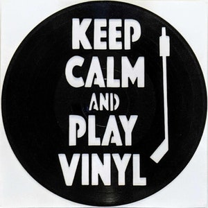 May include: Black vinyl record with white text that reads "Keep Calm and Play Vinyl". A white silhouette of a record player needle is to the right of the text.