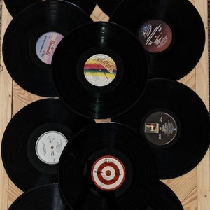 May include: A collection of nine black vinyl records with colorful labels. The records are arranged in a circular pattern on a wooden surface.