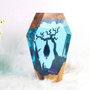 May include: A blue resin sculpture of a tree with a bat hanging from a branch. The sculpture is set in a wooden base.