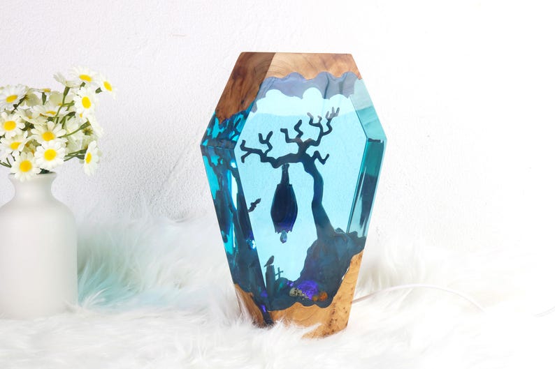 May include: A blue resin sculpture of a tree with a bat hanging from a branch. The sculpture is set in a wooden base.