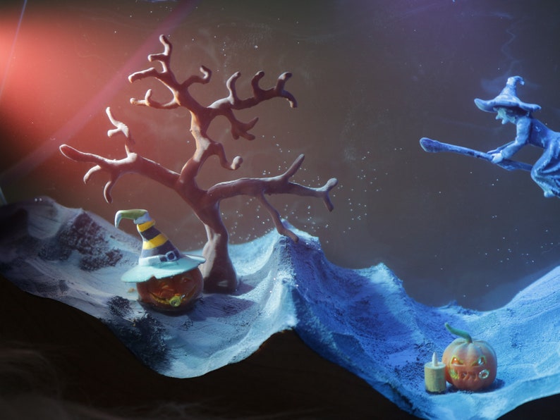 May include: A Halloween scene with a witch flying on a broomstick, a jack-o'-lantern with a witch's hat, and a jack-o'-lantern with a candle. The scene is set against a dark blue background with a white, snowy landscape.