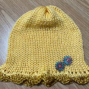 May include: A yellow knitted hat with a scalloped edge and two small blue and yellow flower embellishments.