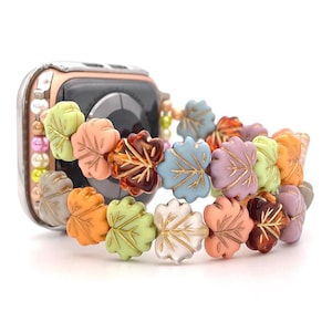 May include: A colorful watch band made of small leaf-shaped beads in various shades of green, orange, pink, and brown. The beads are strung together to create a layered, autumnal design.