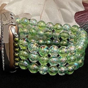 May include: A green iridescent beaded watch band for an Apple Watch. The band is made of multiple strands of beads, creating a layered effect.