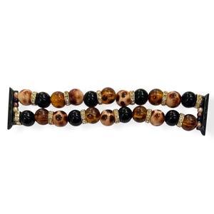May include: A beaded Apple Watch band featuring alternating black, brown, and leopard-print beads. The band includes gold-colored spacers with clear rhinestones. The watch band is designed to fit a standard Apple Watch.