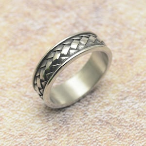 Könnte beinhalten: Ein silberner Ring mit einem geflochtenen Design. Das Band ist breit und das Flechtmuster ist erhaben.