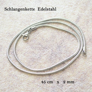 Könnte beinhalten: Eine silberfarbene Schlangenkette aus Edelstahl mit einem Karabinerverschluss. Der Text "Schlangenkette Edelstahl" und "45 cm x 2 mm" ist sichtbar und gibt das Material, die Länge sowie die Dicke des Schmuckstücks an.