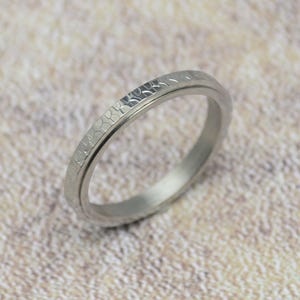 Könnte beinhalten: Ein silberner Ring mit einer strukturierten, gehämmerten Oberfläche. Der Ring ist schlicht und elegant.