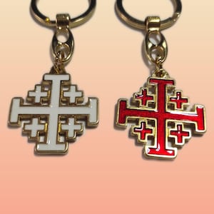 Pode incluir: Dois porta-chaves com cruz de Jerusalém e molduras de metal dourado. Um porta-chaves apresenta um embutido de esmalte branco, enquanto o outro apresenta um embutido de esmalte vermelho. Cada cruz está ligada a um anel circular dourado.