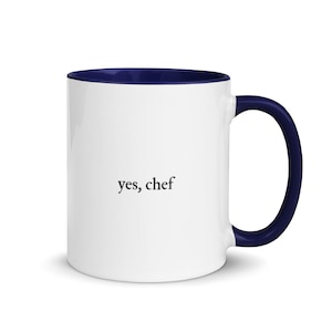 May include: White ceramic coffee mug with a navy blue rim and handle. The mug has the text "yes, chef" printed on the front.