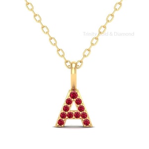 May include: A gold necklace with a pendant in the shape of the letter A. The letter is made of gold and has red gemstones set into it.