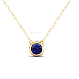 Könnte beinhalten: Eine goldfarbene Halskette mit einem runden, tiefblauen Edelsteinanhänger. Der Anhänger ist in einer goldenen Lünette gefasst und hängt an einer zarten Goldkette. Die Halskette wird vor weißem Hintergrund gezeigt.