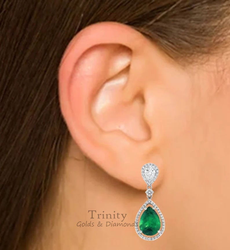 May include: A pair of pear-shaped emerald and diamond drop earrings. The earrings are set in white gold and feature a pear-shaped emerald surrounded by a halo of diamonds. Trinity Golds & Diamonds.