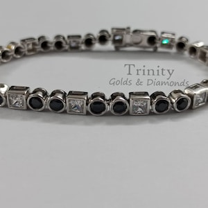 May include: A silver bracelet with alternating black and white round and square stones. The bracelet has a magnetic clasp. The bracelet is from Trinity Golds & Diamonds.
