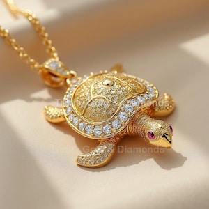 Op de afbeelding: Een gouden schildpad hanger ketting met heldere zirkonia stenen en rode accenten. De schildpad is gedetailleerd met een textuur op de schelp en heeft een ketting.