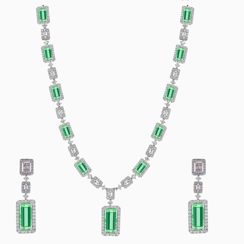 May include: A green gemstone necklace and earrings set with a rectangular emerald cut stone surrounded by smaller diamonds. The necklace has a pendant with a larger emerald cut stone.