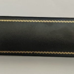 May include: A black rectangular box with a gold decorative border. The box is made of leather and has a smooth surface.