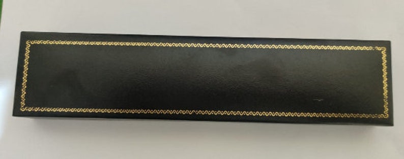 May include: A black rectangular box with a gold decorative border. The box is made of leather and has a smooth surface.