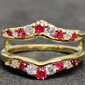 Könnte beinhalten: Ein goldener Ring mit V-förmigem Design, der auf jeder Seite eine Reihe roter und weißer Edelsteine ​​aufweist.