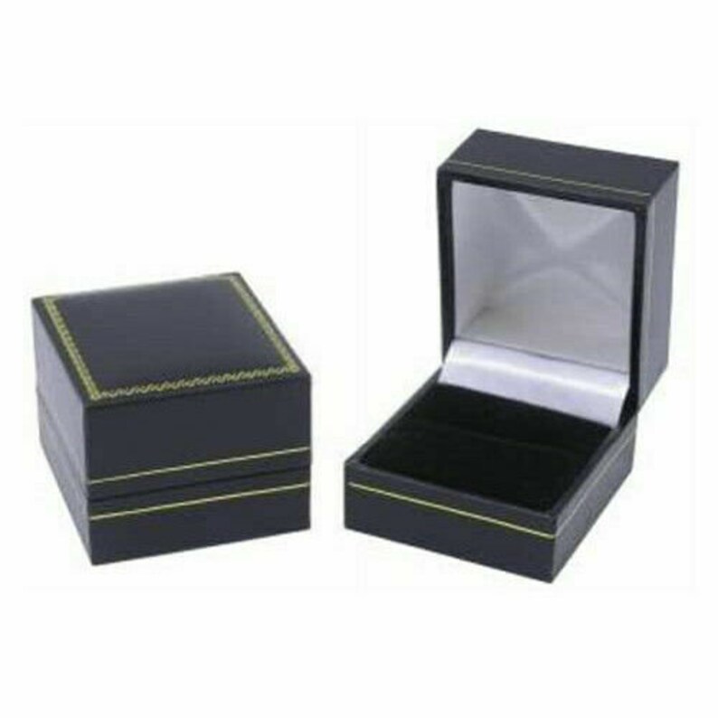 K&ouml;nnte beinhalten: Zwei schwarze Ringboxen mit goldenen Verzierungen. Die Box auf der linken Seite ist geschlossen, w&auml;hrend die Box auf der rechten Seite ge&ouml;ffnet ist und ein schwarzes Samt-Innenleben zeigt.