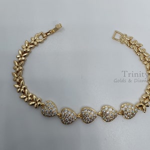 Puede incluir: Un brazalete de oro con un diseño floral y cinco dijes en forma de corazón engastados con piedras transparentes. El brazalete está hecho por Trinity Golds & Diamonds.