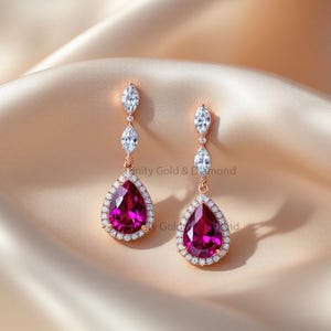 Könnte beinhalten: Ein Paar roségoldene Ohrhänger mit einem birnenförmigen, tiefrosa Edelstein, umgeben von kleinen, klaren Steinen. Die Ohrringe haben drei klare, marquiseförmige Steine, die die Kette hinaufgehen. Präsentiert auf einem satinierten Stoff.
