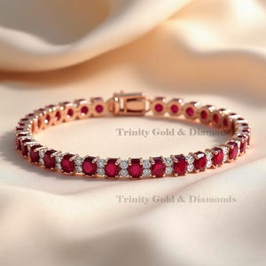 May include: A rose gold bracelet featuring oval-cut red gemstones and small white gemstones. The bracelet is set in a delicate, linked design. The text "Trinity Gold & Diamonds" is visible on the background.