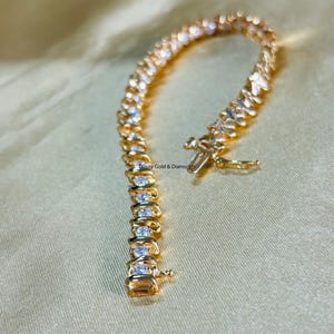 Puede incluir: Un brazalete de oro con una fila de piedras transparentes engastadas en garras. El brazalete tiene un cierre de langosta.