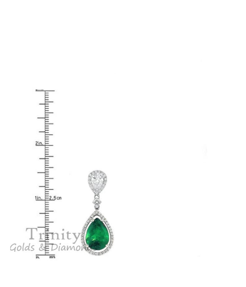 May include: A pear-shaped emerald gemstone earring with a halo of smaller diamonds. The earring is suspended from a smaller pear-shaped diamond with a halo of smaller diamonds. The earring is approximately 2.5 cm long.