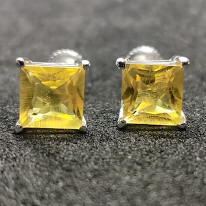 Könnte beinhalten: Ein Paar silberne Ohrstecker mit quadratischen gelben Edelsteinen.